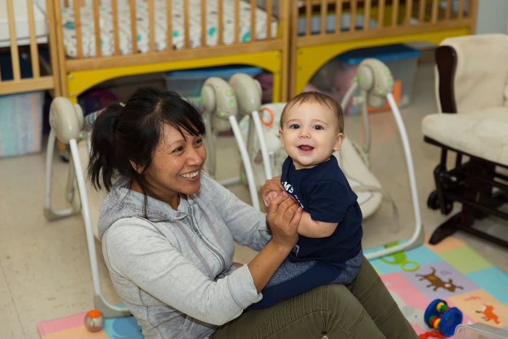 A Wilkins caregiver smiling with a happy baby in the infant room