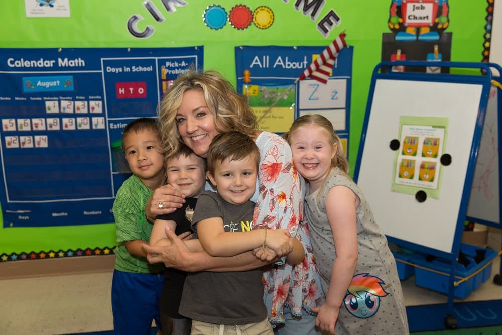 A Wilkins teacher hugging a group of four happy children in the classroom