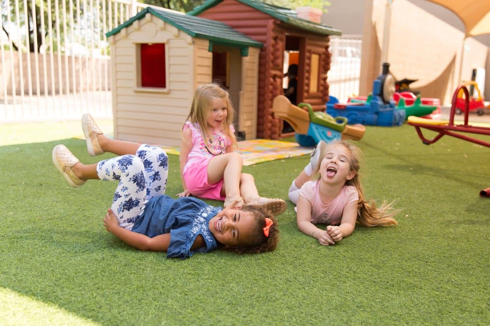 Three preschoolers laughing while playing outside on the playground